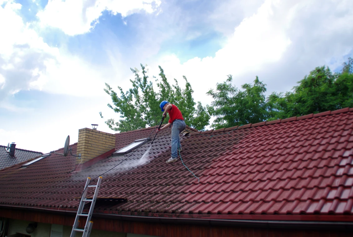 Worker cleaning roof with pressure washer